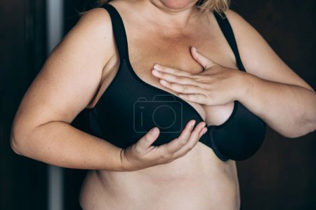 Mujer con sobrepeso y gran tamaño mamario que realiza un autoexamen para el cáncer de mama, una rutina de salud vital para la detección temprana y la conciencia.