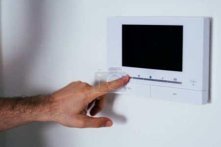 Man finger pressing a button on a wall-mounted home security system, emphasizing safety in residential spaces.