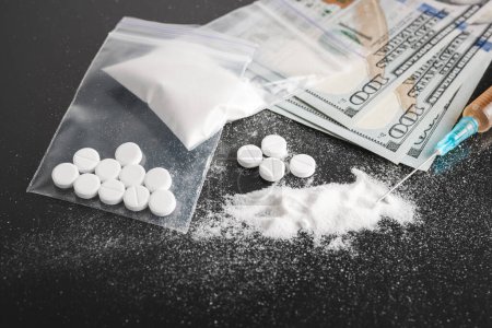 Drugs on dark background, cocaine or heroin white powder, white pills, syringe with a dose and us dollar cash. Drug abuse and addiction concept.