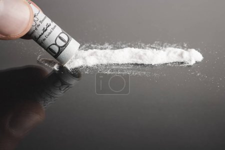 Esnifar cocaína, línea de polvo blanco, billete de dólar enrollado, fondo negro.