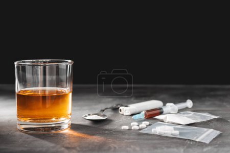 Photo for Alcohol drink in a glass, syringe with a dose of drugs, white pills in a transparent bag and narcotics powder in a spoon on dark background. Concept of addiction and bad habits. - Royalty Free Image