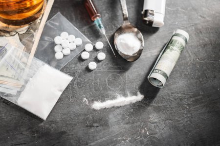 Línea de narcóticos blancos en polvo, pastillas blancas, jeringa con una dosis de drogas y billetes en dólares sobre fondo oscuro. Concepto de adicción y malos hábitos.