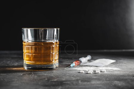 Alcohol drink in a glass, syringe with a dose of drugs, white pills and narcotics powder in a transparent bag on dark background. Concept of addiction, abuse and bad habits.