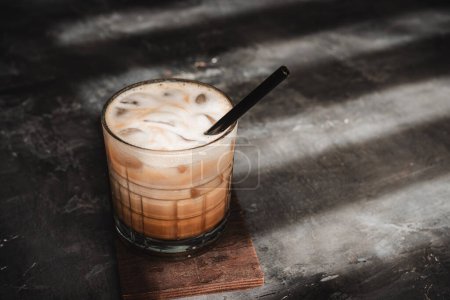 Ice latte coffee drink in a glass with a straw on dark background, summer refreshment drink.
