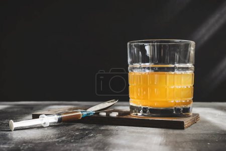 Foto de Beber alcohol en un vaso, jeringa con una dosis de drogas, pastillas blancas y narcóticos en polvo sobre fondo oscuro. Concepto de adicción, abuso y malos hábitos. - Imagen libre de derechos