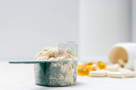 Photo for Whey protein powder in measuring spoon, white capsules of amino acids, vitamins and yellow capsules omega 3 on white background, healthy eating and bodybuilding food supplements. - Royalty Free Image