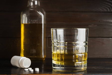 Photo for Alcohol drink in a glass and white pills narcotics, drug dose on wooden table. Concept of addiction and bad habits. - Royalty Free Image