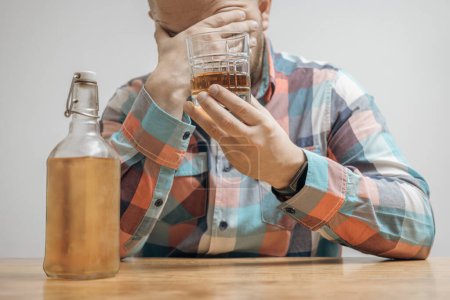 Hombre adicto y borracho en la mesa con un vaso de bebida alcohólica, whisky o brandy, alcoholismo y malos hábitos concepto.
