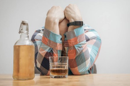 Hombre adicto y borracho en la mesa con un vaso de bebida alcohólica, whisky o brandy, alcoholismo y malos hábitos concepto.
