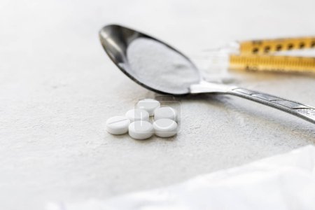 Betäubungsmittel in einem Löffel, Dopingpulver in einer durchsichtigen Plastiktüte, Spritzen mit Medikamenten und weiße Pillen auf einem strukturierten Hintergrund. Konzept von Sucht und schlechten Gewohnheiten.