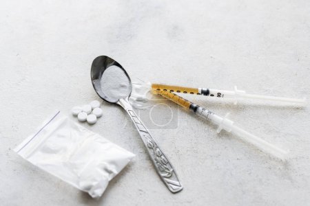 Photo for Narcotic substances in a spoon, dope powder in transparent plastic bag, syringes with dose of drugs and white pills on a textured background. Concept of addiction and bad habits. - Royalty Free Image
