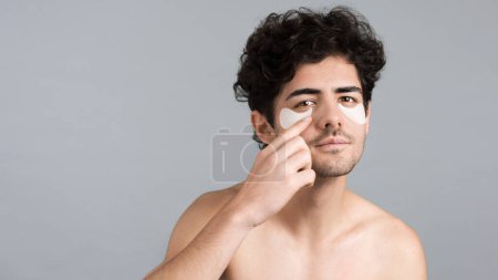 Téléchargez les photos : Un jeune homme caucasien avec barbe de chaume plaçant des taches sous ses yeux, regardant dans la caméra - en image libre de droit