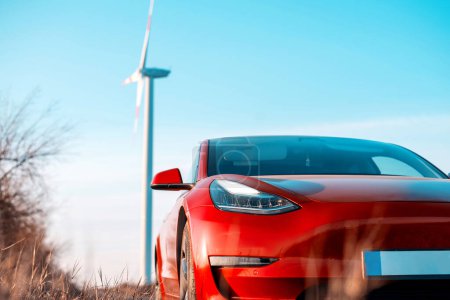 Photo for View of a parked red electric car. Wind turbine on the background - Royalty Free Image
