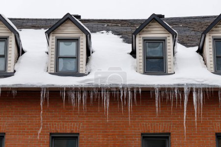 Téléchargez les photos : Residential house with windows on roof covered with snow and hanging icicles in winter. - en image libre de droit