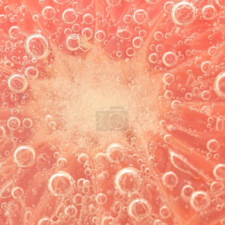 Slice of grapefruit in sparkling water. Grapefruit slice covered by bubbles in carbonated water. Grapefruit slice in water with bubbles.