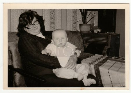 Téléchargez les photos : LA RÉPUBLIQUE SOCIALISTE TCHÉCOSLOVAQUE - CIRCA 1970 : La photo rétro montre la grand-mère berce un petit bébé. Photographie vintage noir et blanc. - en image libre de droit