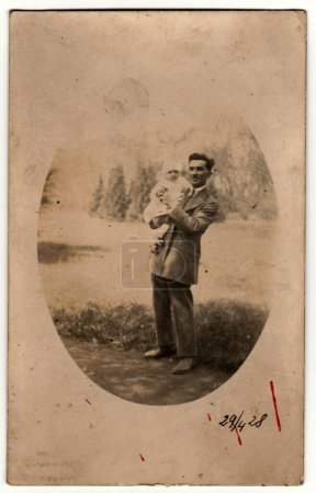 Téléchargez les photos : PRAHA (PRAGUE), RÉPUBLIQUE TCHÉCOSLOVAQUE - 29 AVRIL 1928 : Une photo vintage montre un petit bébé bercé par un homme. Photographie noir et blanc rétro. Vers les années 1930. - en image libre de droit