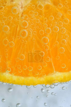 Foto de Rebanada de fruta naranja madura en agua sobre fondo blanco. Primer plano de fruta naranja en líquido con burbujas. Rebanada de fruta naranja madura en agua con gas. Macro imagen de fruta en agua carbonatada - Imagen libre de derechos