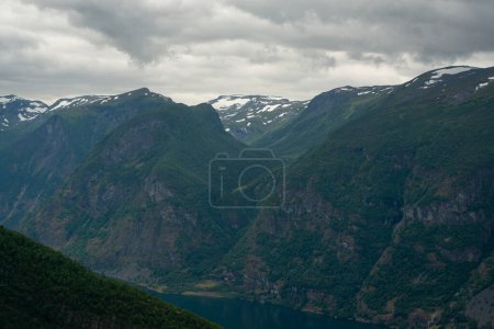 Naturblick auf die norwegischen Berge mit weißer Schneedecke auf der Höhe vom Stegastein-Aussichtspunkt an einem bewölkten Sommertag. Blaue UV-Strahlung in den Bergen.