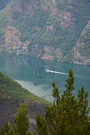 Blick auf einen norwegischen Gebirgsfluss mit klarem, blauem Wasser, auf dem sich eine weiße Privatjacht bewegt.