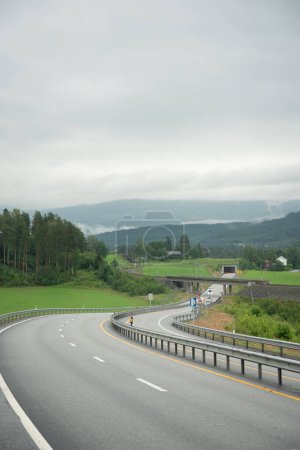 highway in Norway with four lanes leading into a tunnel through the mountains. Cloudy day with white fog in the mountains.