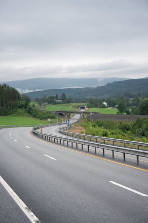 highway in Norway with four lanes leading into a tunnel through the mountains. Cloudy day with white fog in the mountains.