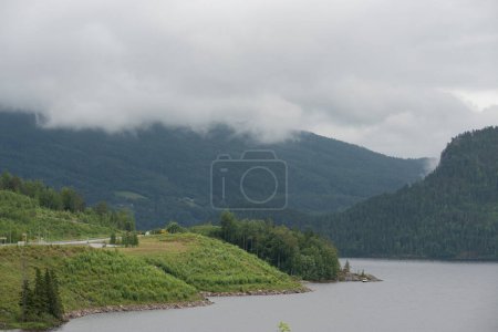 Fluss in Norwegen fließt an nebligen Tagen entlang von Bergen mit grünen Bäumen und neben einer Autobahn.