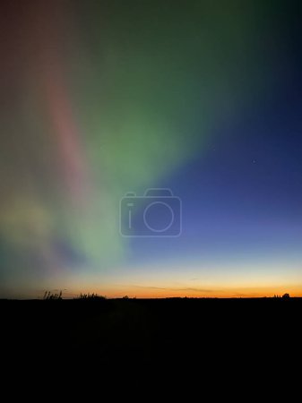 Northern lights over forest with sunset in the horizon