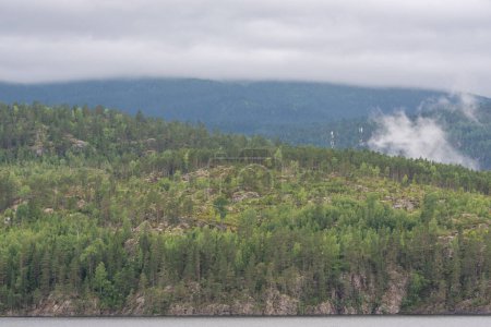 Téléchargez les photos : Beau paysage avec des montagnes de fjord norvégien rocheux sur lesquels poussent des cumulus blancs et des conifères verts sur la rive du lac - en image libre de droit