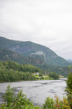 Beautiful landscape with a view of Norwegian mountains with green coniferous trees under a blue sky on the river bank.