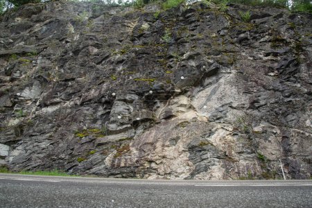 steinige Felswand neben einer Bergstraße, in die zur Sicherheit Metallbefestigungen gebohrt wurden.