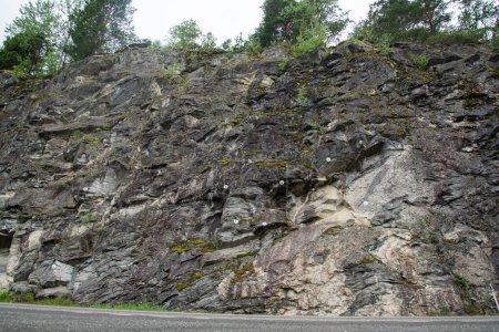 steinige Felswand neben einer Bergstraße, in die zur Sicherheit Metallbefestigungen gebohrt wurden.