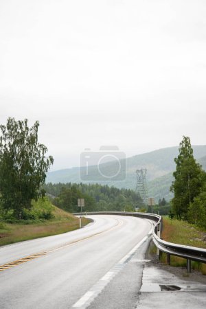 Bergstraße in Norwegen mit Metallbarrieren in einer scharfen Kurve. Berge sind in der Ferne zu sehen.