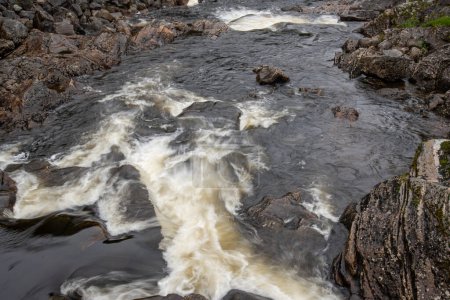 Nahaufnahme eines felsigen Gebirgsflusses, wo das Wasser auf die Felsen trifft und weißen Schaum bildet.