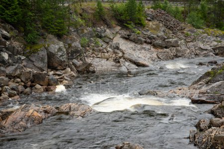 Nahaufnahme eines felsigen Gebirgsflusses, wo das Wasser auf die Felsen trifft und weißen Schaum bildet.