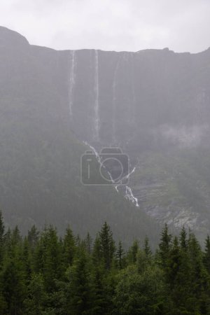 huge waterfall falling from a Norwegian mountain peak on a foggy rainy summer day.