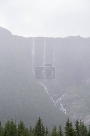 enorme cascada que cae de un pico de montaña noruega en un día lluvioso niebla verano.