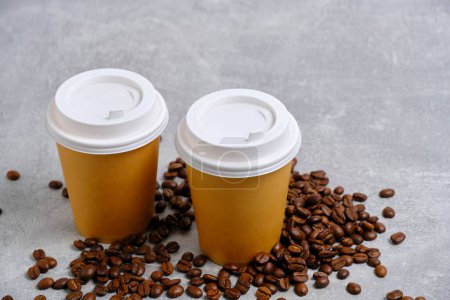 Téléchargez les photos : Deux tasses en papier jetables pour le café chaud reposent sur des grains de café sur fond de béton léger - en image libre de droit