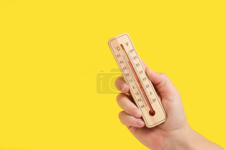 Téléchargez les photos : Main avec thermomètre extérieur sur jaune. Reflète la chaleur brûlante, idéal pour les conseils de sécurité d'été ou les prévisions météorologiques - en image libre de droit