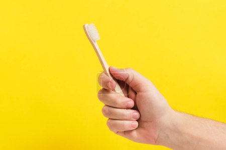 Bambus-Zahnbürste in der Hand auf gelbem Hintergrund, ideal für die Förderung eines umweltfreundlichen Lebensstils oder Mundhygiene-Produkte