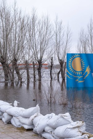 Inondations dans la ville du Kazakhstan en 2024.Sacs de sable et bannière du Kazakhstan noyés dans l'eau de fonte sur fond
