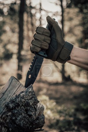Man hand in a military glove holds a knife in the forest