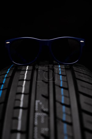 Blue sunglasses on a car tire. Isolated on black background