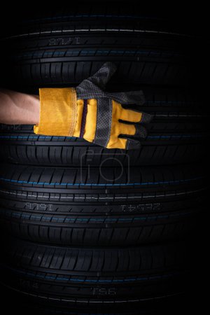 Hand in yellow glove with car tires on black background, closeup. Concept of car service