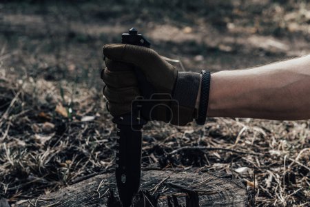 Man hand in military glove holds knife in forest. Concept survival in wild