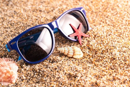 Blaue Sonnenbrille und Muscheln am Strand. Konzept Strandurlaub
