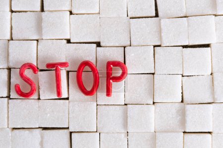 Word STOP spelled out in red letters on background white sugar cubes, emphasizing message against sugar consumption