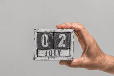Date is July 02. Wooden calendar in hand on gray background