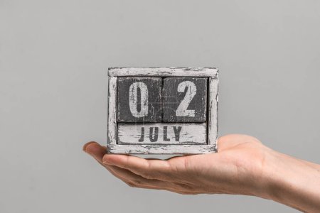 Date is July 02. Wooden calendar in hand on gray background