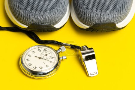 Referees whistle, stopwatch and sneakers on yellow background. Concept of fitness